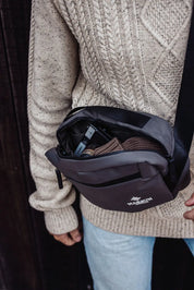 Person wearing a black waist bag with a visible brand logo, holding it open.